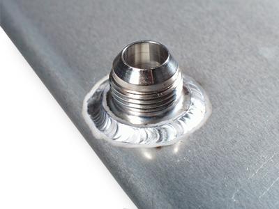 Pro-Werks mild steel male AN weld bung shown welded into a flat gray panel, threaded inlet up, with a TIG weld bead ringing its base